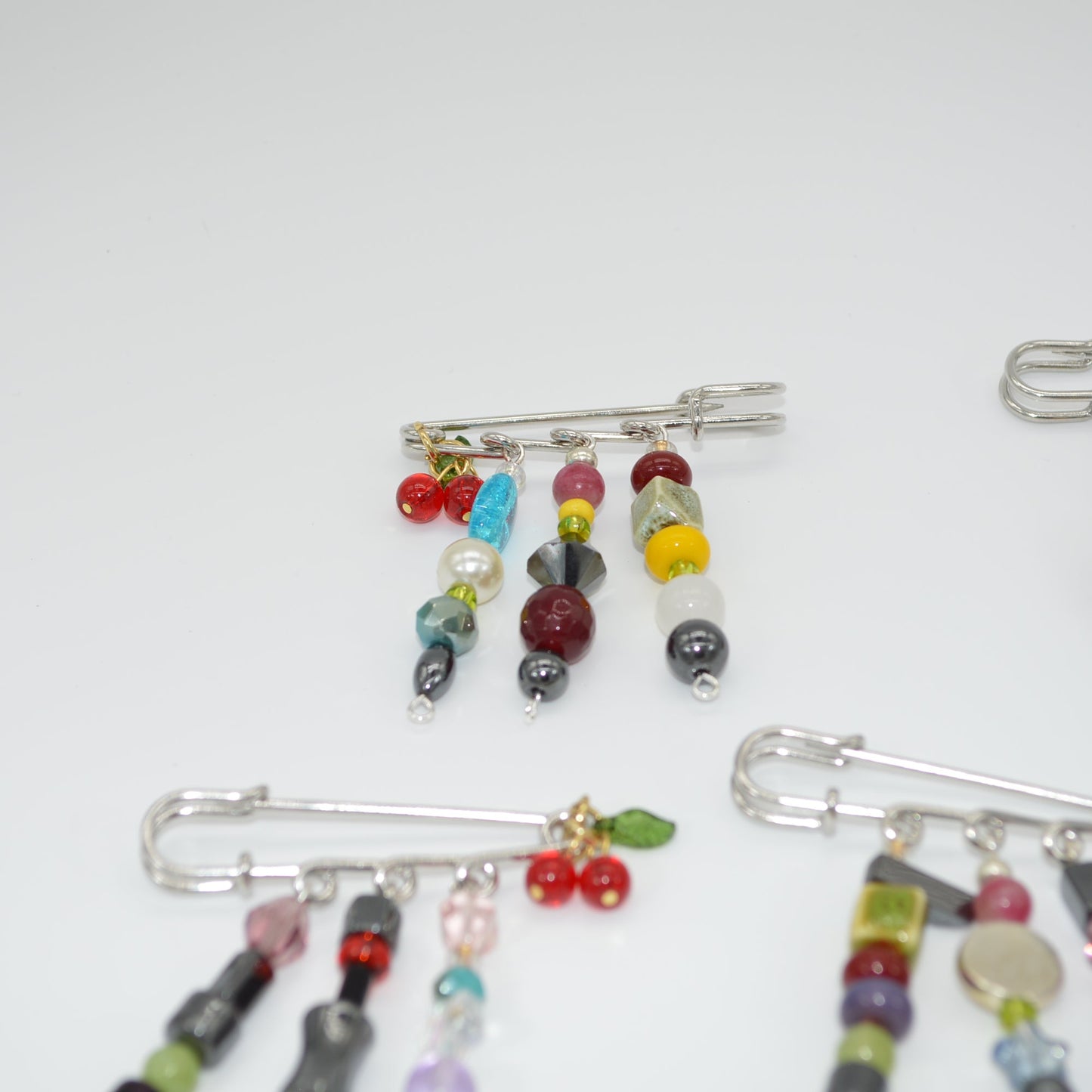 Colorful beaded brooches on safety pins against a white background