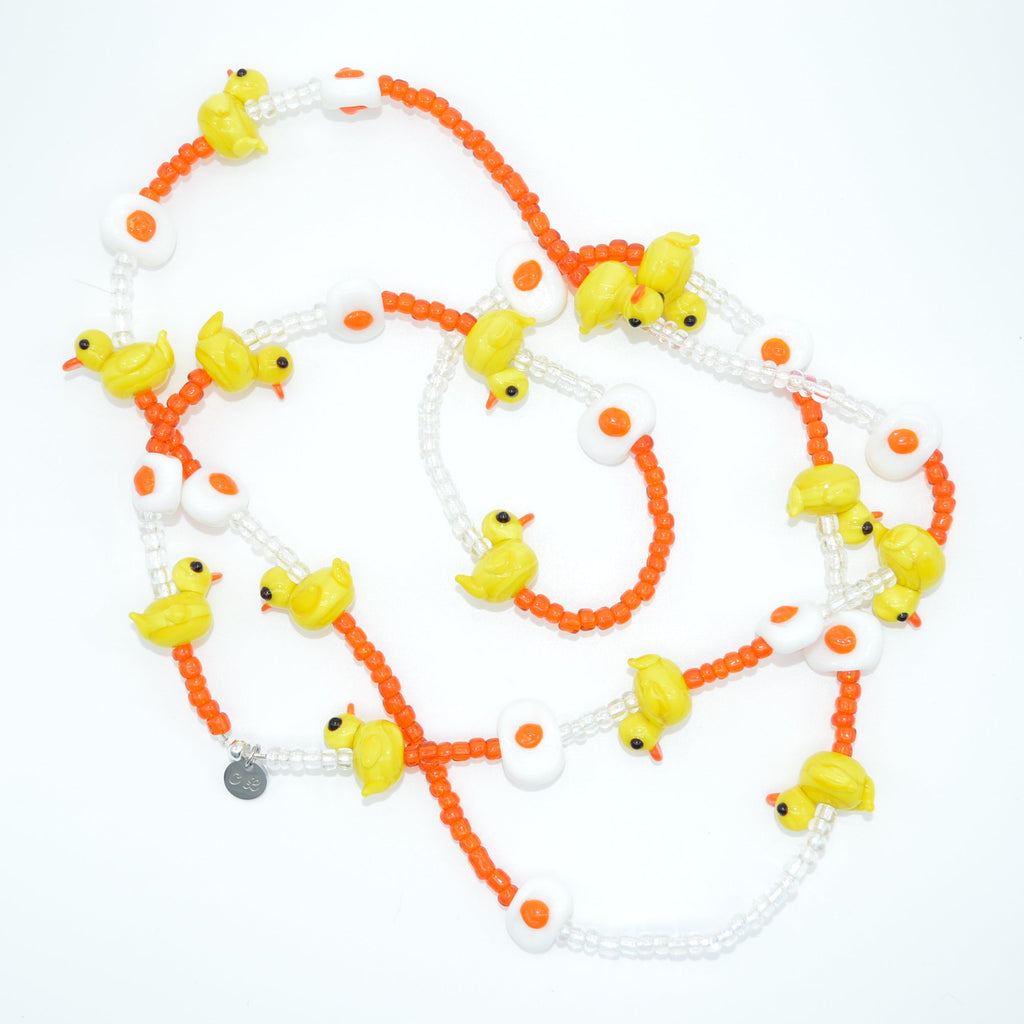 Necklace with yellow duck charms and orange beads on a white background