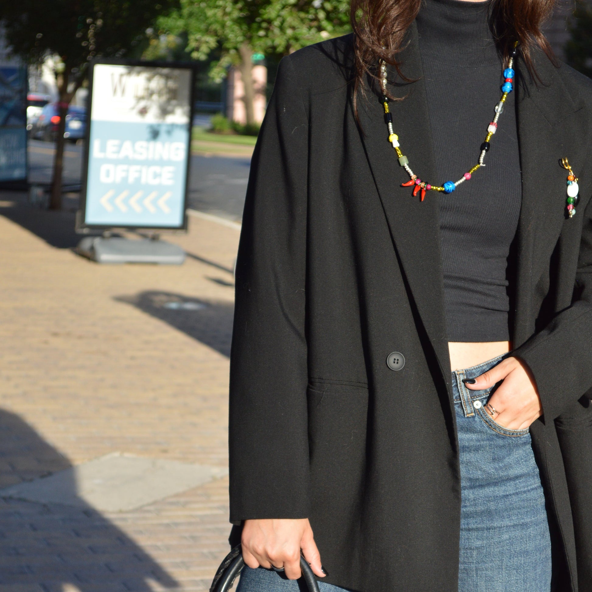 Person holding a black leather handbag with colorful beads on a sidewalk.