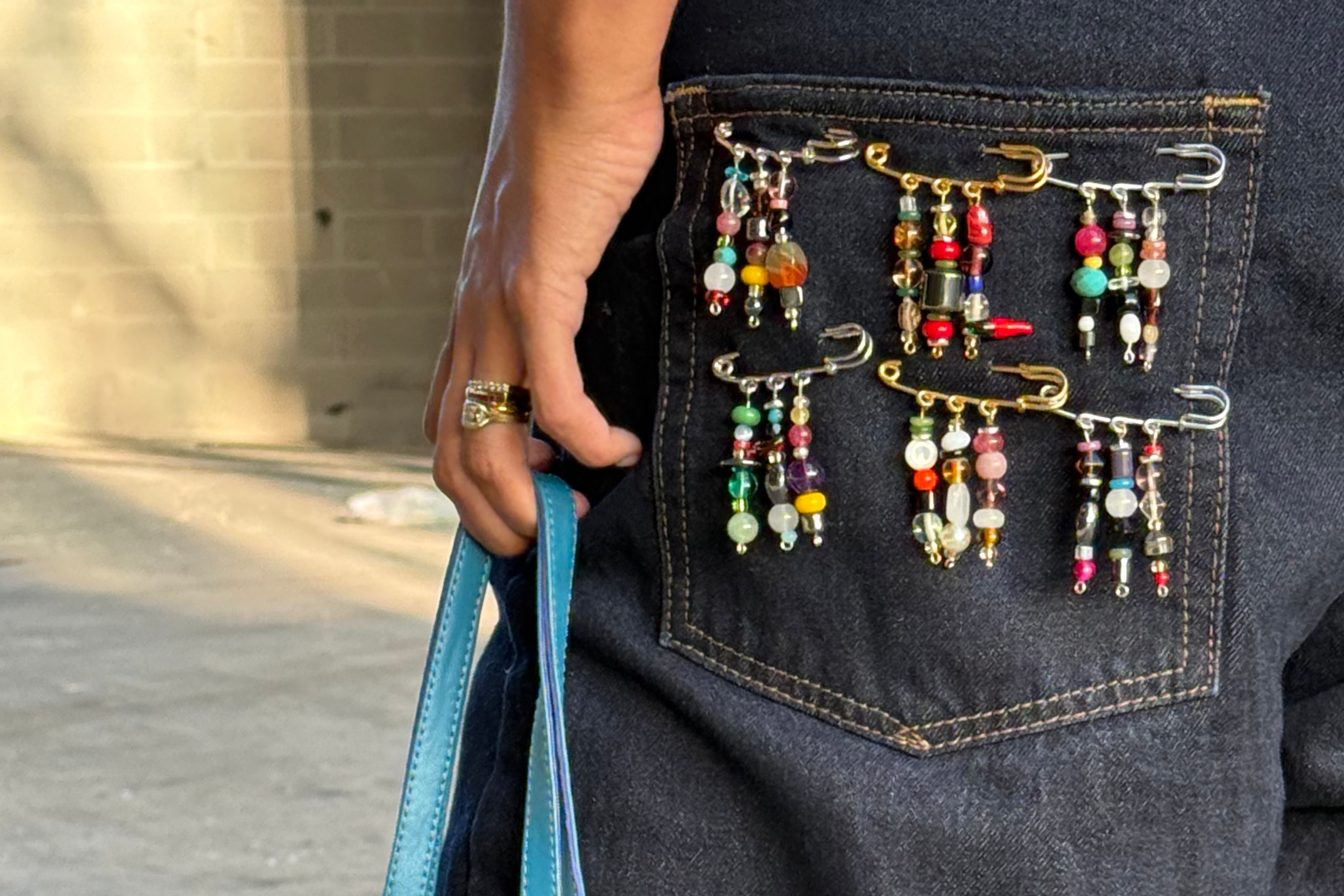 Person holding a blue beaded handbag with colorful jewelry attached, standing against a neutral background.