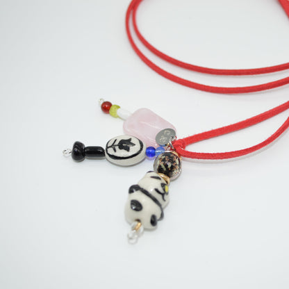 Red cord necklace with panda charm on a white background