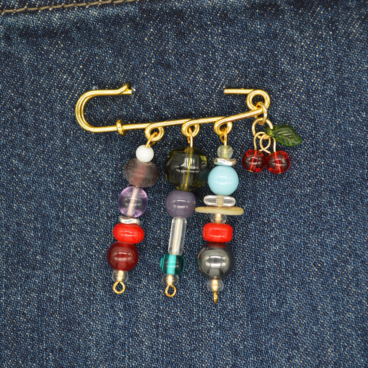 Decorative brooch with beads and charms on a denim background