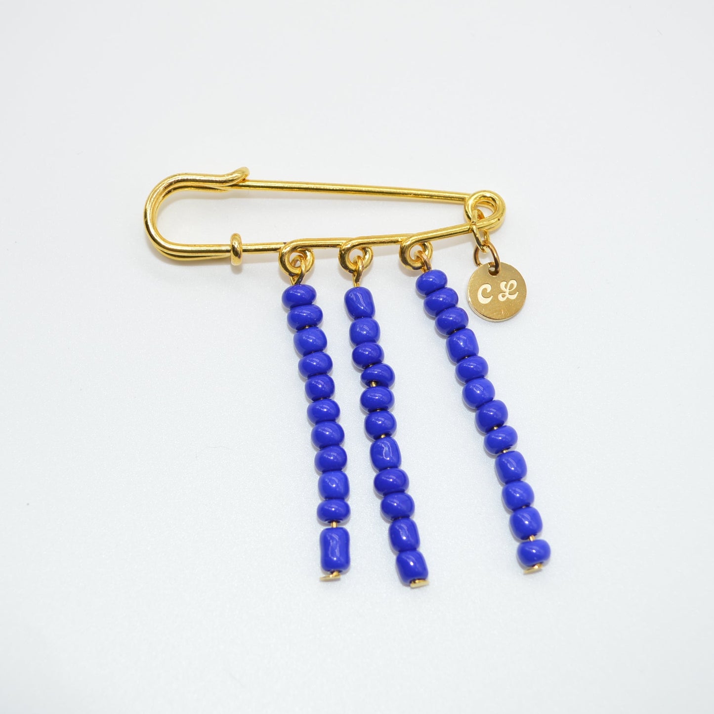 Gold safety pin brooch with blue beads on a white background