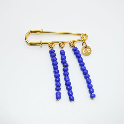 Gold safety pin brooch with blue beads on a white background