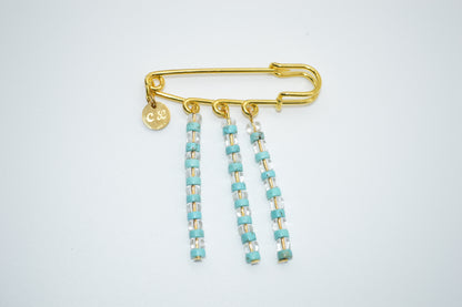 Gold brooch with turquoise beads on a white background