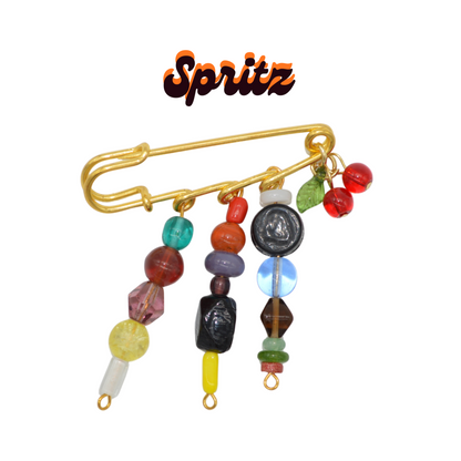 Colorful beaded brooch with a gold clasp on a white background, branded 'Spritz'.