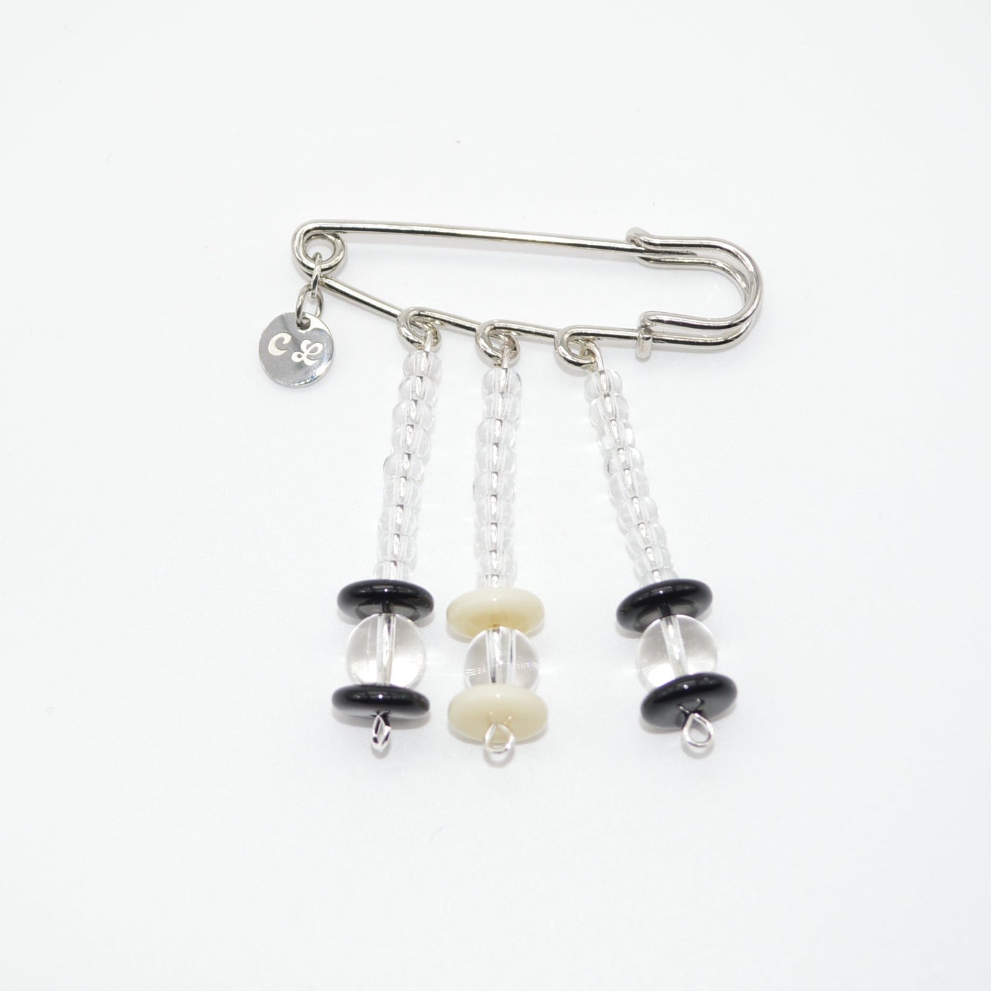 Silver safety pin with black and white beads on a white background