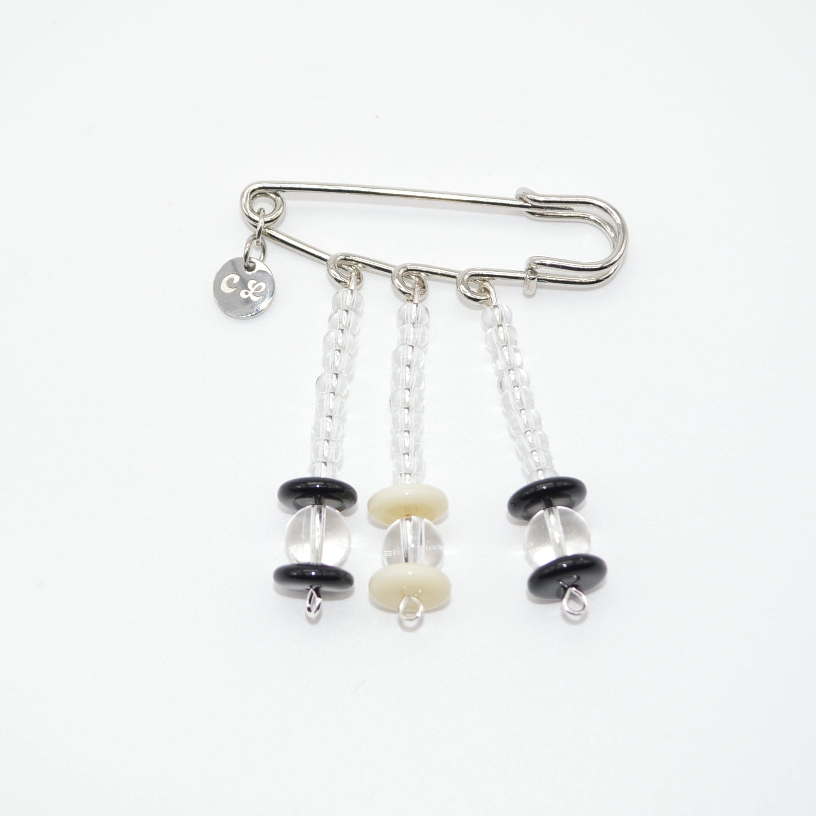Silver safety pin with black and white beads on a white background