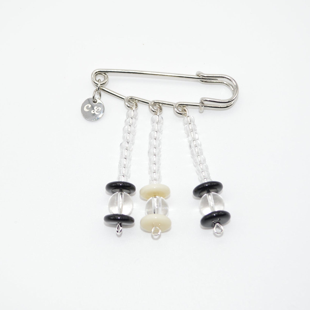 Silver safety pin with black and white beads on a white background