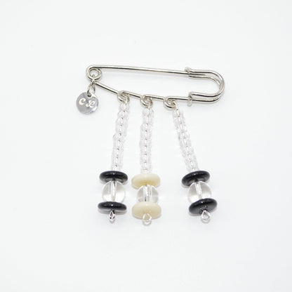 Silver safety pin with black and white beads on a white background
