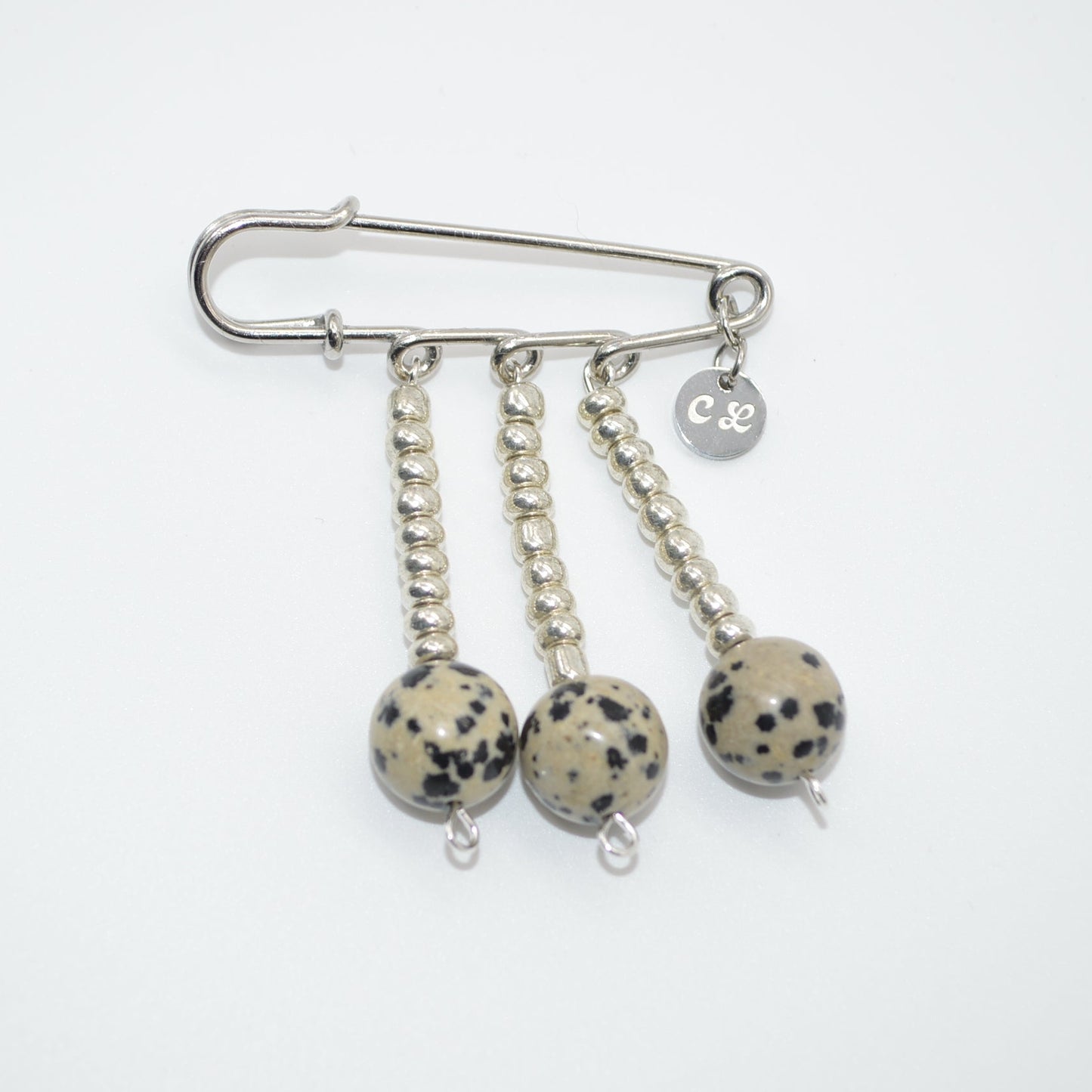 Silver brooch with three dangling balls on a white background