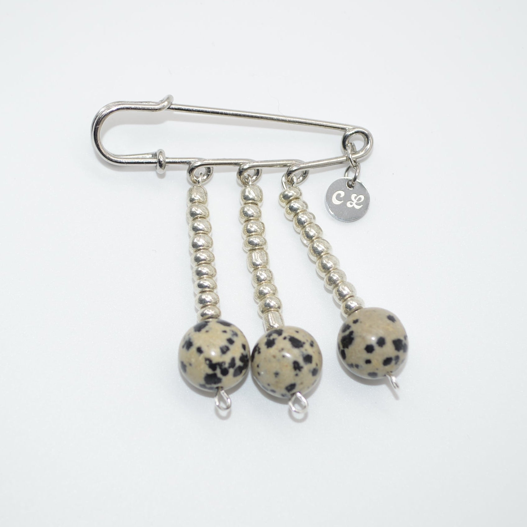 Silver brooch with three dangling balls on a white background