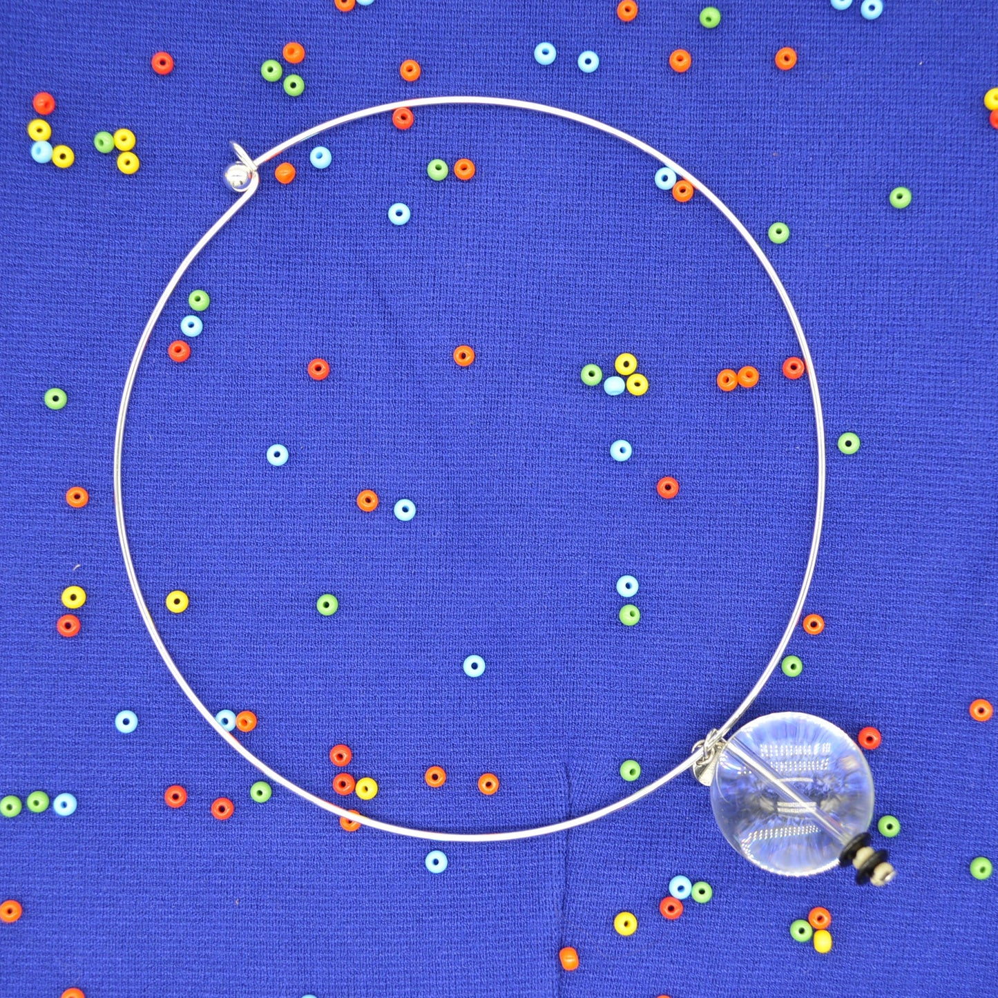 silver choker necklace over blue background with colorful beads. 