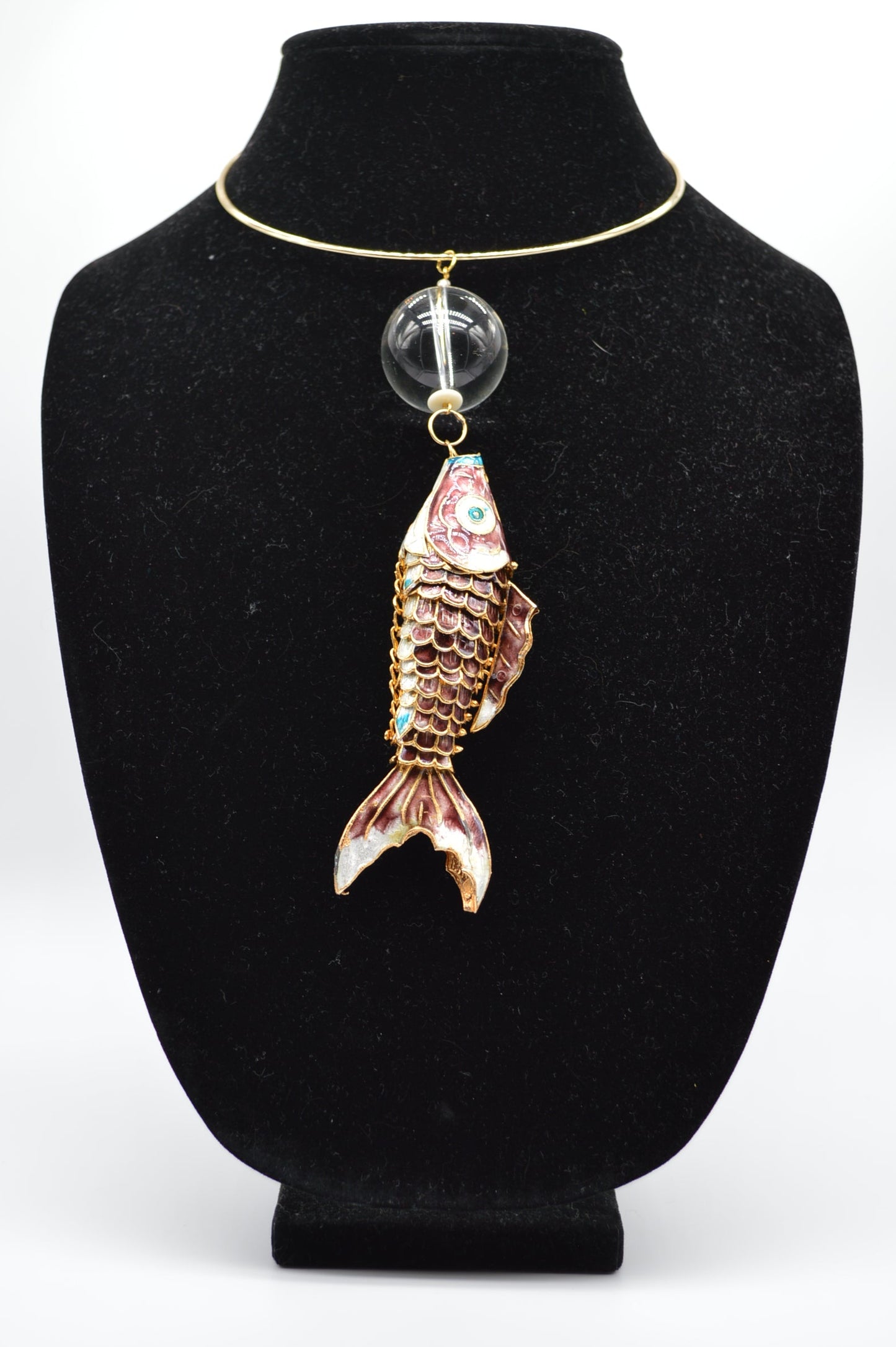 Jewelry display with a fish-shaped pendant on a black stand.