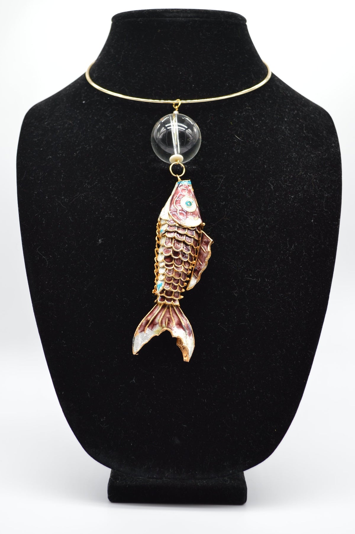 Jewelry display with a fish-shaped pendant on a black stand.