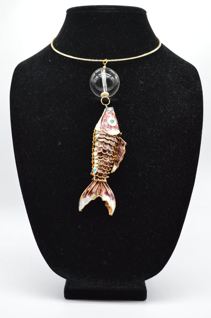 Jewelry display with a fish-shaped pendant on a black stand.