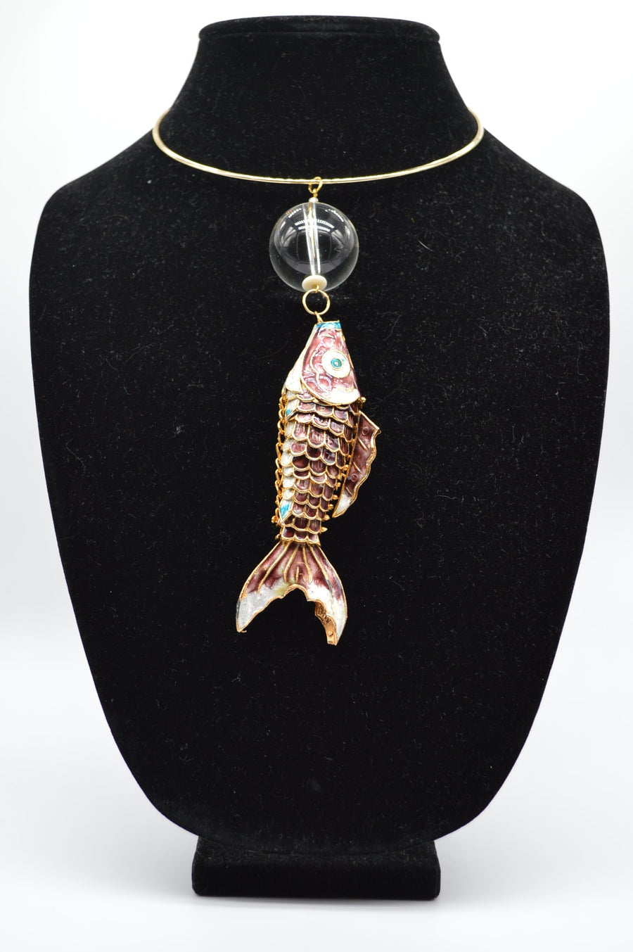 Jewelry display with a fish-shaped pendant on a black stand.