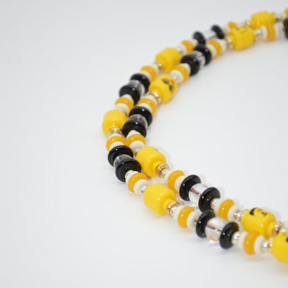 Beaded necklace with yellow, black, and white beads on a light gray background