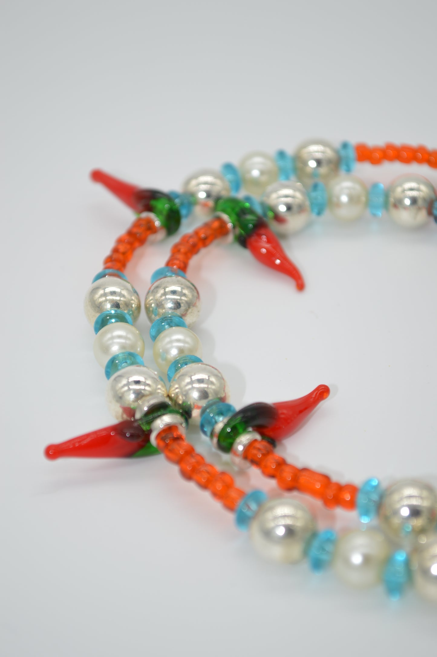 Closer Look at colorful beaded necklace with red, green, and orange accents on a white background
