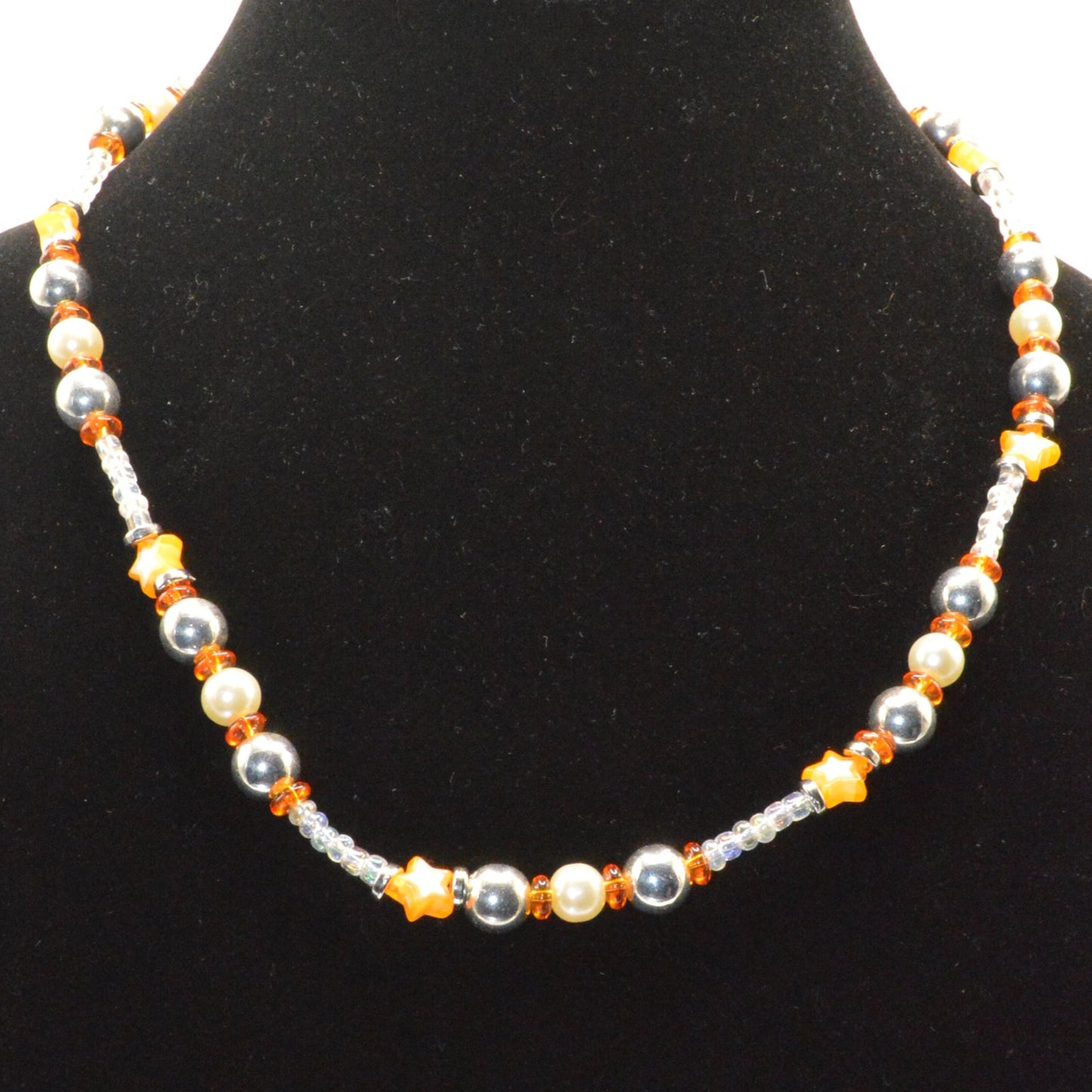 Beaded necklace with orange and silver beads on a black display stand.
