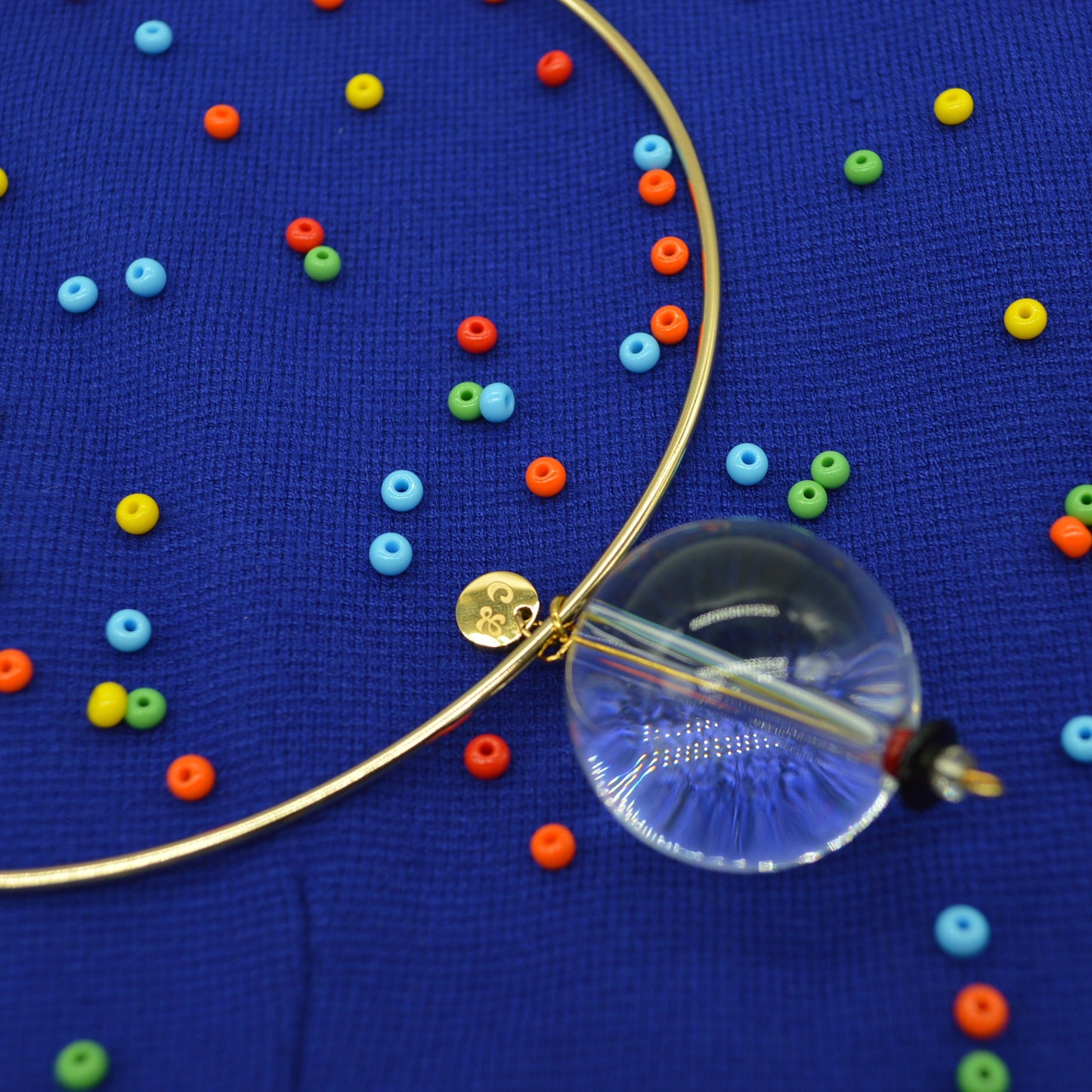 glass orb bead of a necklace on a blue surface with colorful beads scattered around